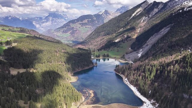 Aerial pullback over Obersee lake surrounded by alpine forests, mountain slopes and panoramic Swiss landscapes near N&auml;fels, Glarus.