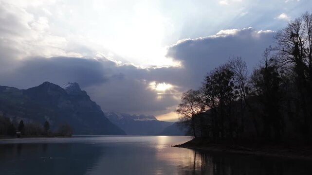 Cinematic drone pullback Walensee lake, alpine mountains, dramatic sunset clouds and shoreline silhouettes in Switzerland.