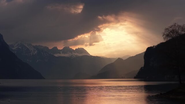Cinematic aerial view of Walensee at sunset with dramatic clouds, alpine mountains and golden reflections on lake.