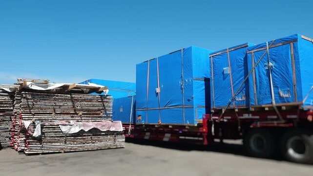 Flatbed trailers loaded with oversized industrial cargo wrapped in protective covers at a logistics yard. Heavy freight transportation, cargo shipping and industrial logistics.