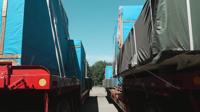 Heavy industrial equipment packed in protective covers on flatbed trailers at a logistics yard. Oversized freight transportation, cargo shipping and industrial supply chain operations.