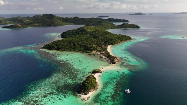 Breathtaking aerial drone clip of a tropical island paradise in Palawan, Philippines. Features a pristine white sandbar beach, turquoise coral reef shallow waters, and lush jungle-covered hills.