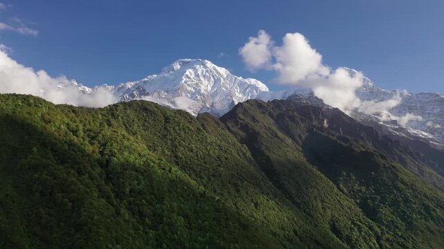 Breathtaking view of the iconic Machapuchare peak and snow-capped Himalayan mountains through a deep, forested valley in Nepal. Features dramatic sunbeams slicing across dark mountain ridges.