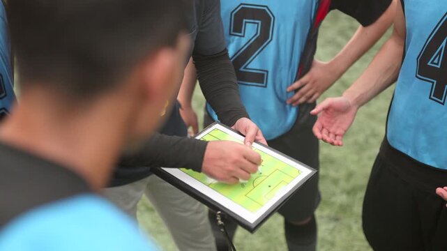 Experienced football coach is teaching goal-scoring techniques and game-changing strategies to his players during training. Teamwork and dedication to the sport are emphasized.
