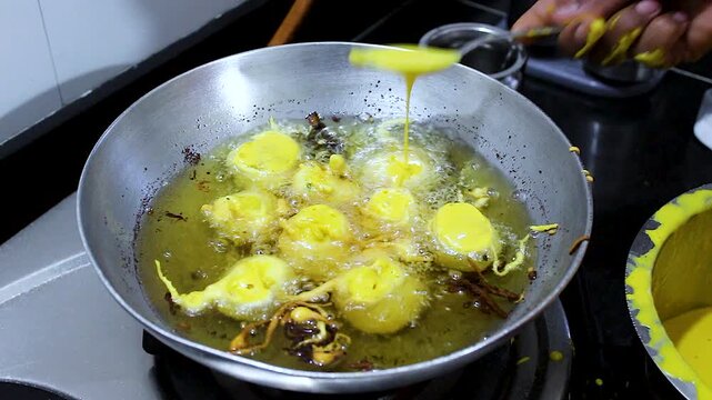Close-up of batata vada deep frying in hot oil with besan batter coating. Ideal for Indian cuisine, street food, cooking tutorials, snack preparation and food culture projects.