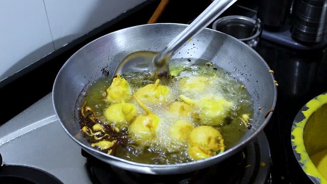 Close-up of batata vada frying in hot oil with slotted spoon stirring. Ideal for Indian street food, cooking tutorials, traditional recipes, snack preparation and food culture content.