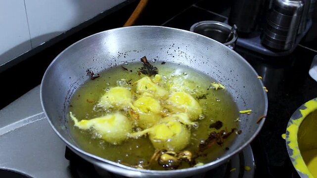 Close-up of batata vada frying in hot oil in home kitchen. Ideal for Indian street food, traditional recipes, cooking tutorials, food culture and snack preparation content.