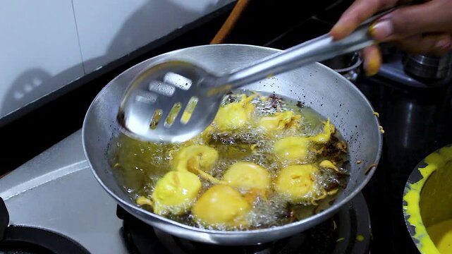 Close-up of batata vada being deep fried in hot oil on kitchen stove. Ideal for Indian cuisine, street food, cooking process, snack preparation and food culture content.