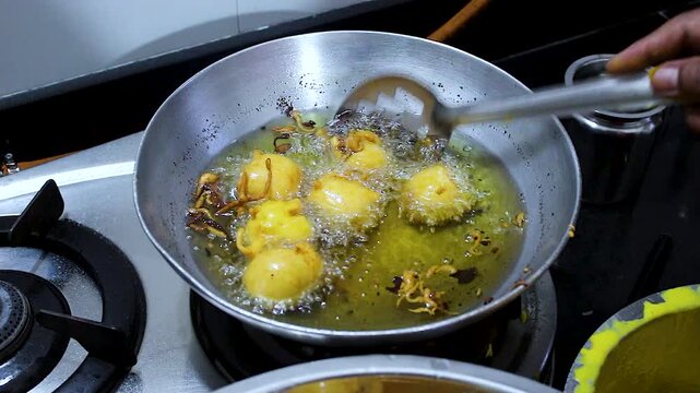 Close-up of batata vada being deep fried in hot oil and lifted from pan. Ideal for Indian street food, snack preparation, cooking tutorials, restaurant, and food culture content.