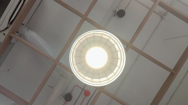 Dynamic rotating upward shot of bright ceiling light fixture in modern commercial building. Ideal for workplace, retail, architecture, infrastructure, and interior design projects.
