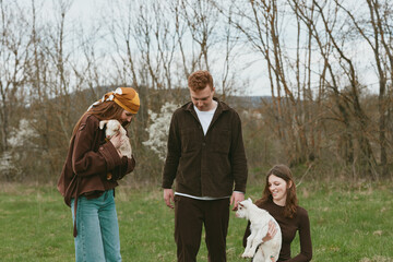 Obraz premium An outdoor family moment with a young goat kid in a field, one adult kneels to pet the kid while others smile nearby, creating a candid lifestyle scene of animal companionship and rural bonding.