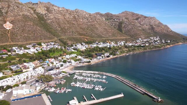 Gordon's Bay harbour and yacht marina with exclusive real estate on mountainside. Stunning drone view of seaside coastal town overlooking False Bay in South Africa
