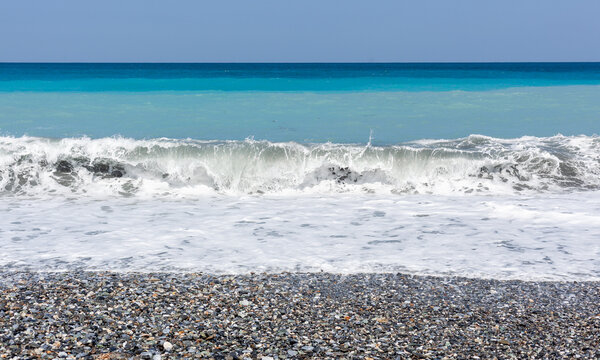 Pacific Ocean waves crashing on a pebble beach in Hualien, Taiwan. Clear blue sky over the coastal landscape. Natural scenery at the shore.