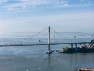 Fototapeta premium San Francisco Bay Bridge eastern span structure, traffic moving across its decks, and ships navigating the calm bay waters under a clear sky