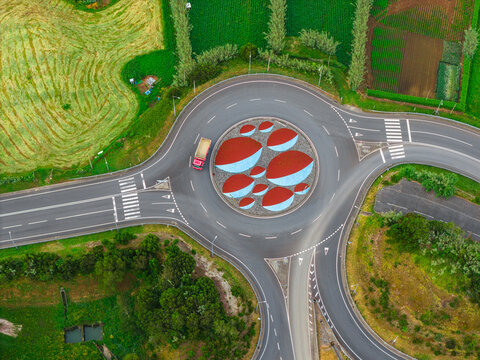 Aerial view of the roundabout in Agua de Pau featuring a unique red and blue art installation surrounded by lush green agricultural fields in Agua de Pau, Azores, Portugal.