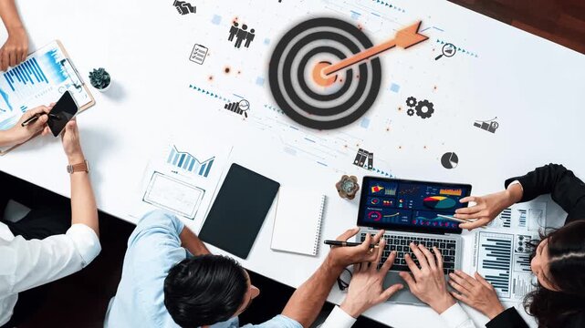 A top-down view of a collaborative business meeting showcasing a team analyzing charts and data on multiple devices, emphasizing goal-oriented strategies and teamwork. Raster