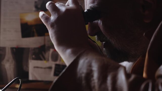 A detective monitors a target through binoculars in a shadowy operations room. The scene evokes surveillance, criminal investigation, intelligence gathering, and suspenseful thriller narratives.
