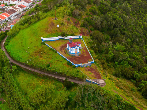 Aerial view of Ermida de Nossa Senhora do Monte chapel situated on a grassy hill surrounded by lush vegetation and overlooking the town of Agua de Pau, Azores, Portugal.