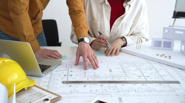 Engineering team collaborating on architectural blueprints, reviewing construction plans, and discussing building design concepts with tools and safety hard hat on table