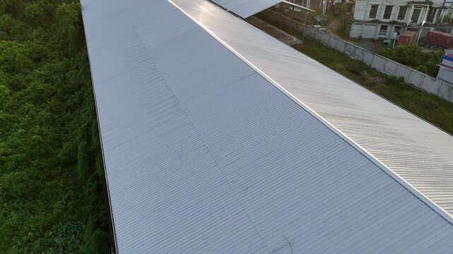 An aerial view from the roof of a metal warehouse with corrugated panels overlooking a green field and an industrial storage area