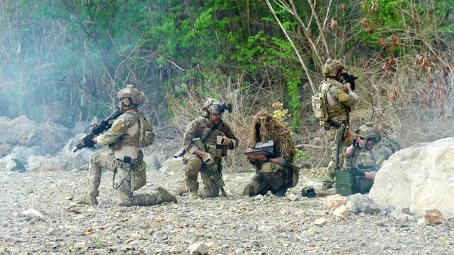 Armed soldiers conduct tactical maneuvers during military training exercises in a natural outdoor environment