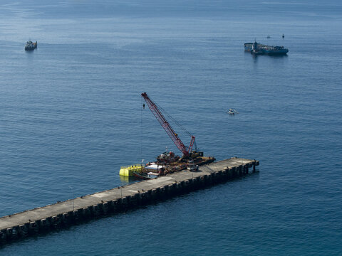 Aerial view of the Oil Fuel Terminal Port featuring a crane barge docked at the concrete jetty surrounded by the deep blue sea, Manggis, Bali, Indonesia.