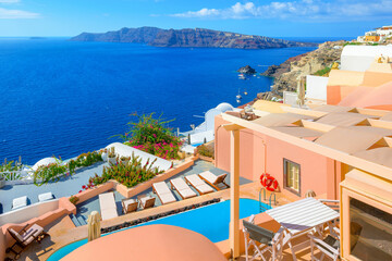 Obraz premium Pastel coral colored cave houses and resort terraces with sea views and swimming pools above the whitewashed town of Oia, on the island of Santorini, Greece.