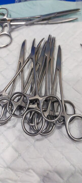 Pile of stainless steel surgical scissors and hemostatic forceps on a white medical pad, ready for a clinical procedure.