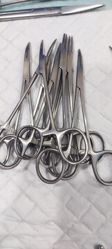 Pile of stainless steel surgical scissors and hemostatic forceps on a white medical pad, ready for a clinical procedure.