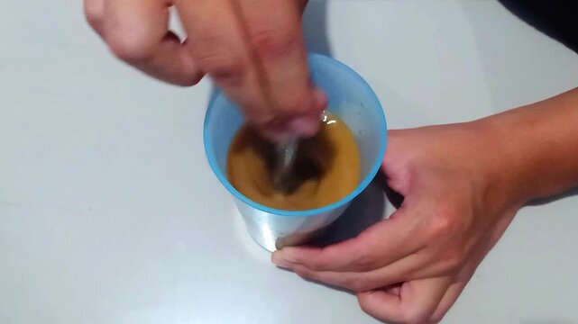  Indramayu - Indonesia - Saturday, June 27, 2026 - The process of stirring coffee in a blue plastic cup and adding ice cubes to it.