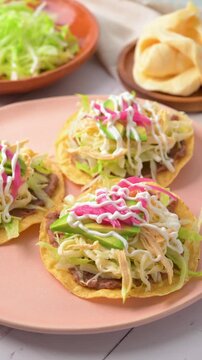 Close up of Mexican tostada topped with shredded chicken, quesillo, cream and pickled onions