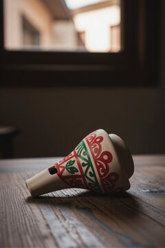 A handcrafted wooden whistle with intricate red and green painted patterns rests on a wooden surface in a modern minimalist interior.