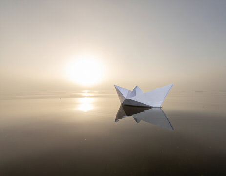 single paper boat drifting across still water in soft morning fog symbolizing dreams, hope and exploration.