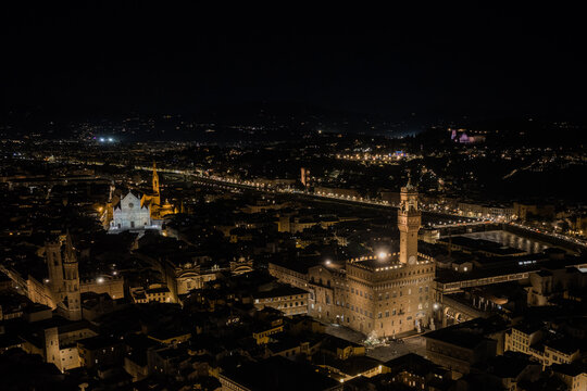 Aerial view of the illuminated Palazzo Vecchio and the Basilica of Santa Croce at night, showcasing the historic architecture and city lights of Florence, Tuscany, Italy.