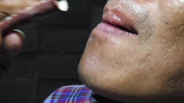 Close up of an Asian man sanding his artificial tooth using a piece of sandpaper inside his mouth