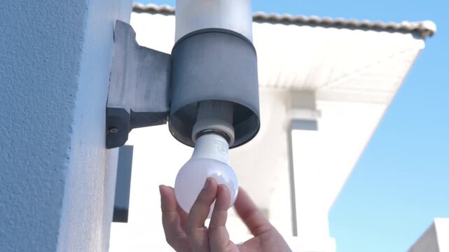 Close up shot of a person hand replacing or installing an energy-saving LED light bulb into an outdoor wall lamp fixture of a residential building