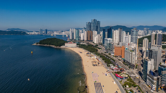 Aerial view of Haeundae Beach with its sandy shore, rows of umbrellas, and the modern skyline of skyscrapers in Busan, South Korea.