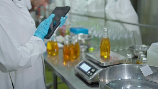 Laboratory technician measuring ingredients for beverage production with digital scale and tablet in modern factory setting