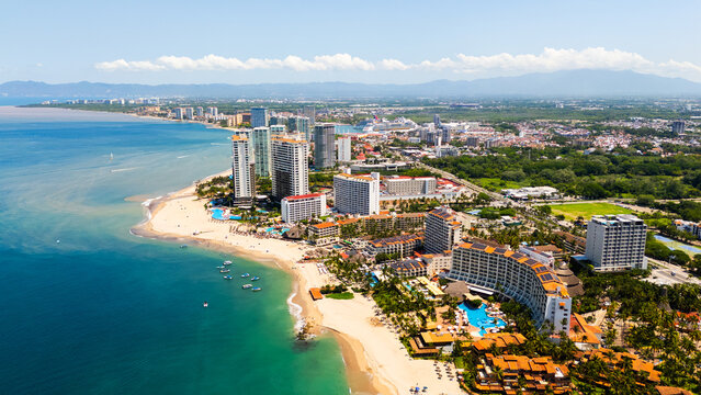 Aerial view of the Puerto Vallarta skyline featuring high-rise hotels, sandy beaches, turquoise ocean waters, and lush green vegetation in Puerto Vallarta, Jalisco, Mexico.