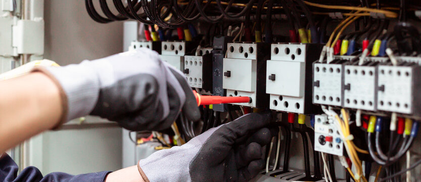 Close-up of electrician hands installing and testing electrical circuit breaker in control panel.