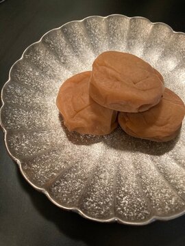 Three pickled plums Umeboshi on a traditional silver plate with black background