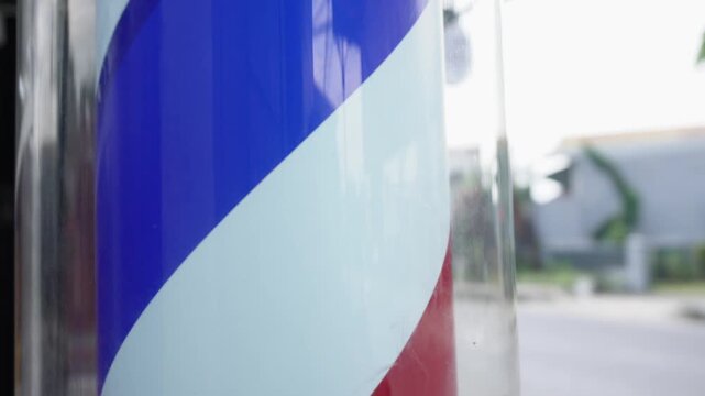 Close up view of a traditional vintage barber pole with red, white, and blue spiral stripes, classical sign symbol for barbershop, men's grooming salon, or hair cutting service business.