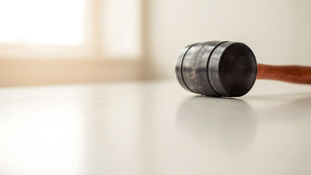 A black rubber mallet placed on a smooth white surface indoors