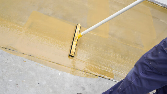 A construction worker spreading liquid resin coating on a concrete floor surface