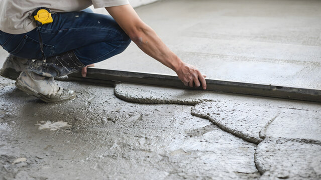 Construction worker leveling wet concrete floor using a metal screed tool