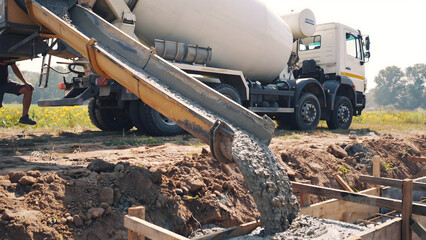 Fototapeta premium Concrete mixer truck pouring liquid cement into a foundation trench at a construction site