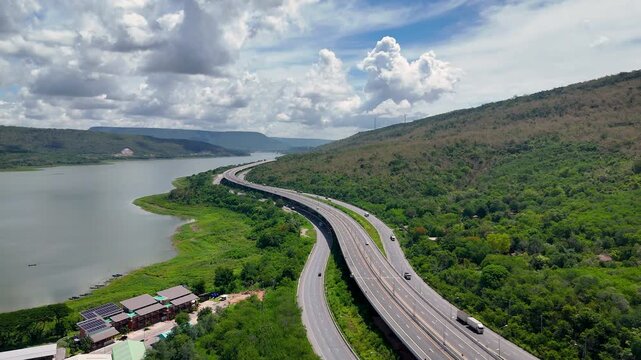 Aerial view of highway running along river and green hills. Transportation, infrastructure, travel and logistics concept