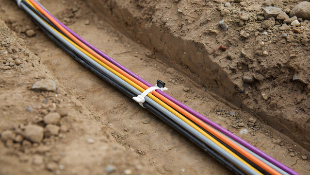 Colored fiber optic cables installed inside an open trench in the ground