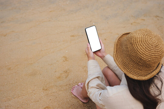 Top view mockup image of a woman holding mobile phone with blank desktop screen on the beach