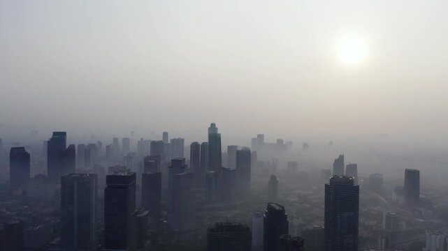 Aerial view of a city skyscraper skyline enveloped in dense morning fog or heavy smog under a hazy sun.